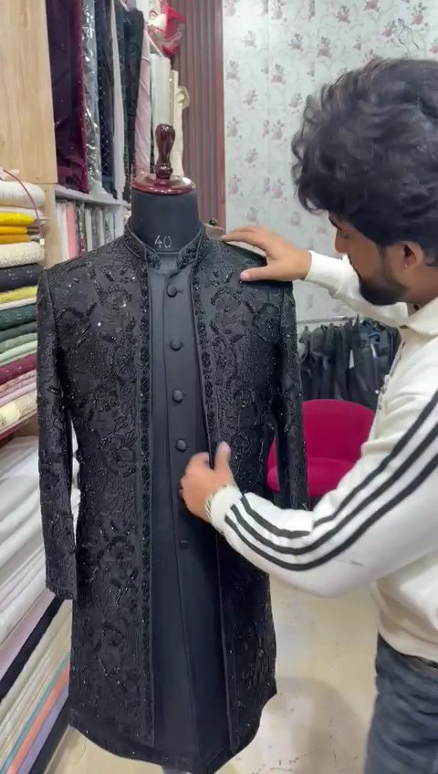A tailor fitting a black embroidered bandhgala on a stand