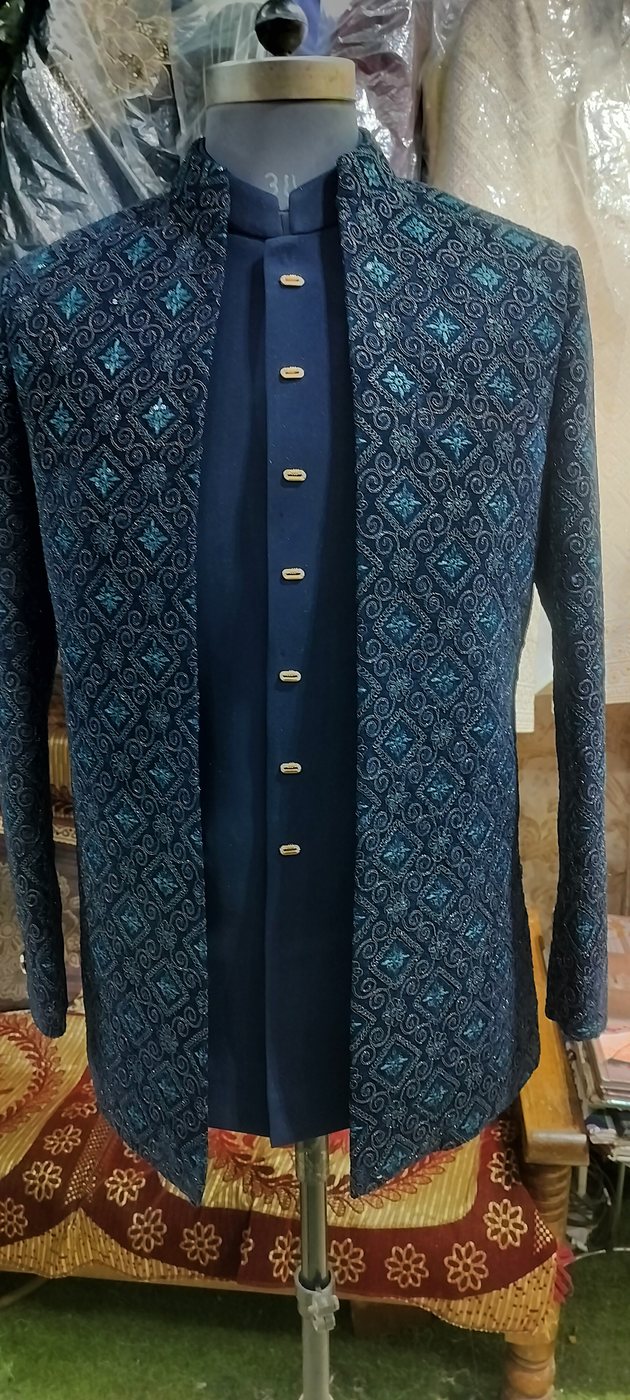 A teal brocade open-front jacket over a navy kurta with gold buttons, on a stand