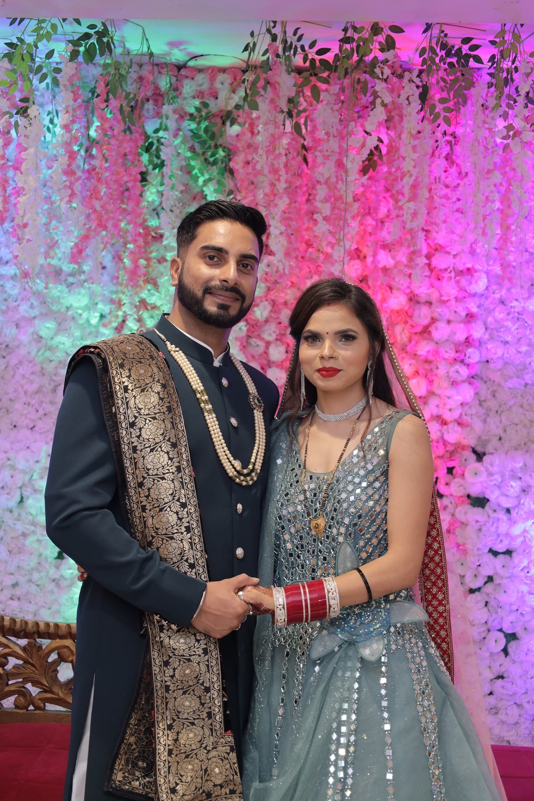 A couple at their wedding, the groom in a black sherwani with a gold dupatta
